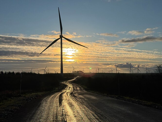 Sun reflecting on the Spine Road with a silhouetted wind turbine